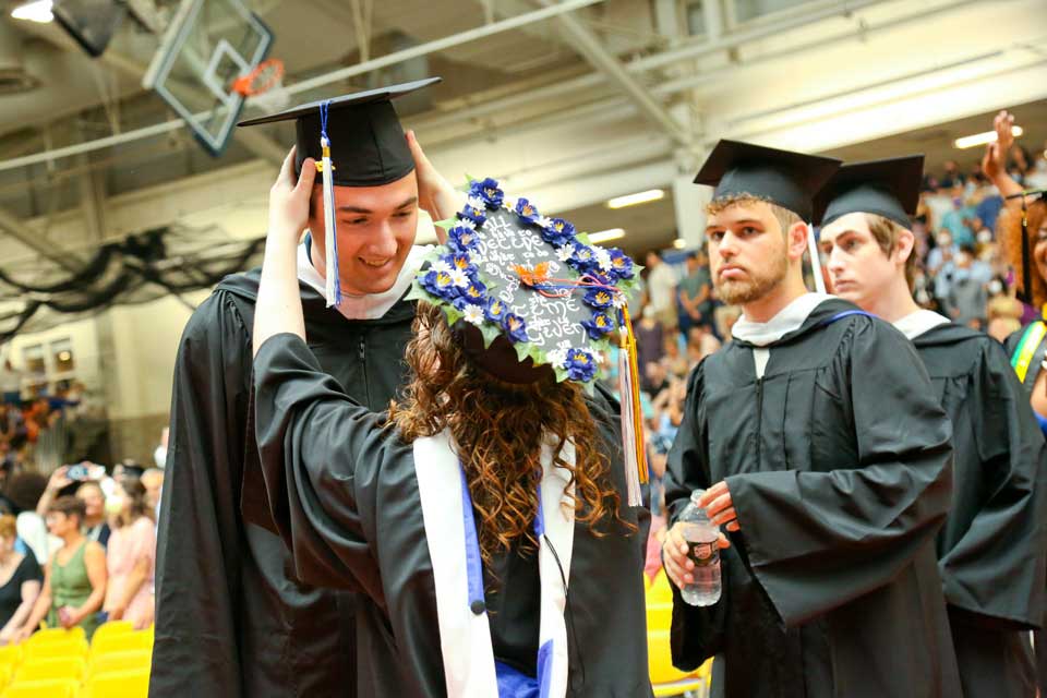 A graduate fixes a fellow graduate's cap at commencement