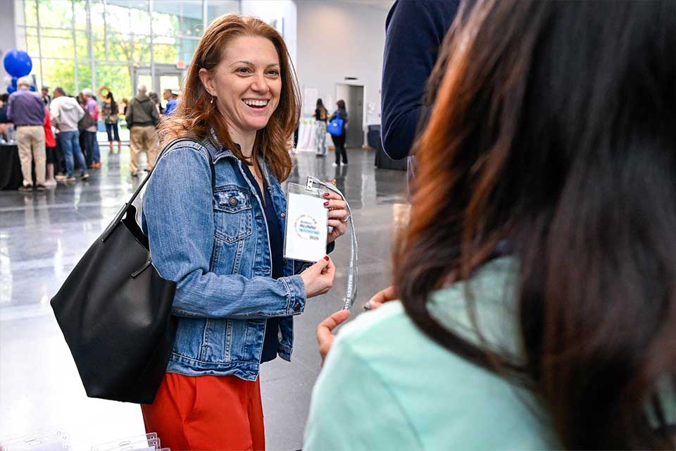 Woman smiling, holding her registration badge for alumni weekend